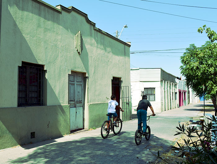 Niños andan en bicicleta por una vereda frente a una casa antigua
